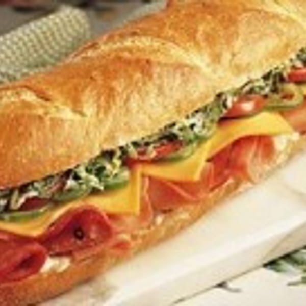 A large submarine sandwich with various meats, cheeses, and vegetables on a baguette.