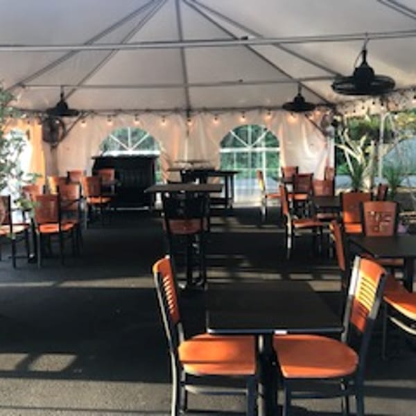 Outdoor dining area under a white tent with orange chairs and black tables.