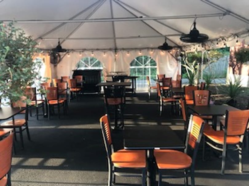 Outdoor dining area under a white tent with orange chairs and black tables.