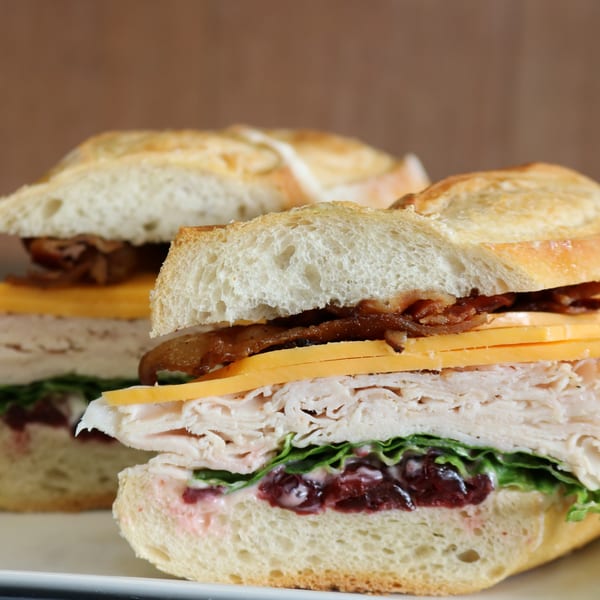 Two turkey sandwiches on baguettes with cheese, bacon, lettuce, and cranberry sauce.