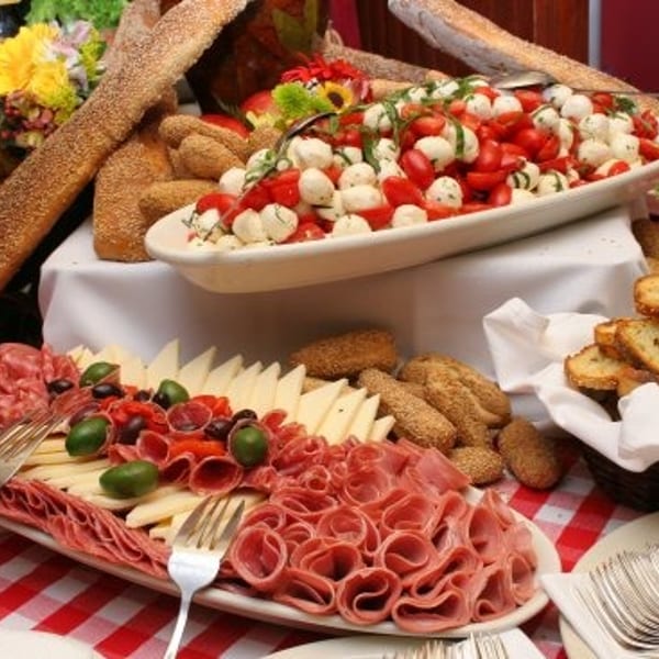 A buffet table laden with charcuterie, cheese, caprese salad, baguettes, and toasted bread.