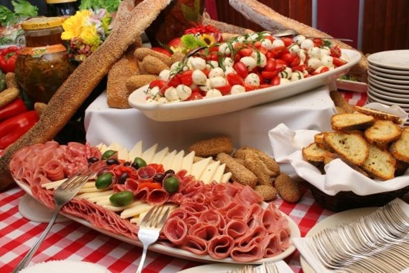 A buffet table laden with charcuterie, cheese, caprese salad, baguettes, and toasted bread.