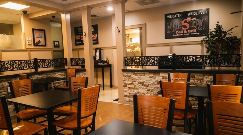 Interior of Main Street Deli & Grill with empty tables, chairs, and a catering sign.