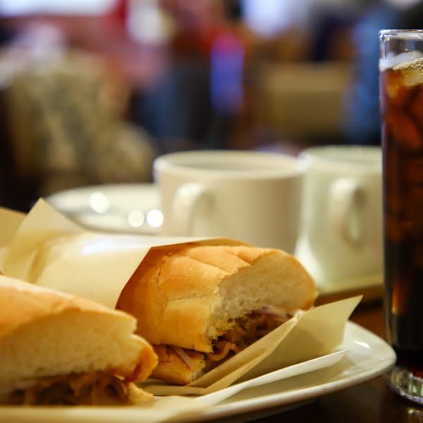 Two sandwiches wrapped in paper on a plate next to a glass of iced cola.
