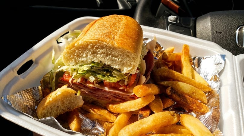 A large deli sub sandwich with lettuce, tomato, and meats, served with golden french fries.