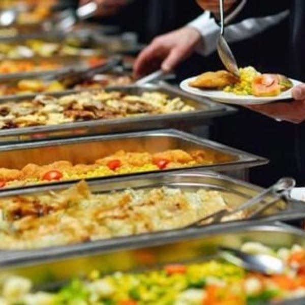 People serving themselves from a buffet line with various hot dishes in chafing dishes.